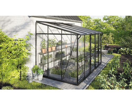 Gewächshaus aus Glas und Metall mit Pflanzenregalen im Garten.