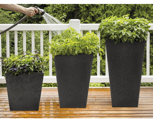Drei Pflanzkübel aus Kunststoff in unterschiedlichen Größen mit Pflanzen werden mit einem Gartenschlauch bewässert.