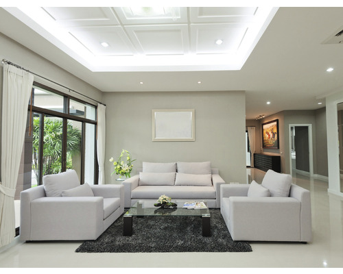 Helles Wohnzimmer mit Sofa, Sesseln und Glas Couchtisch auf einem Teppich