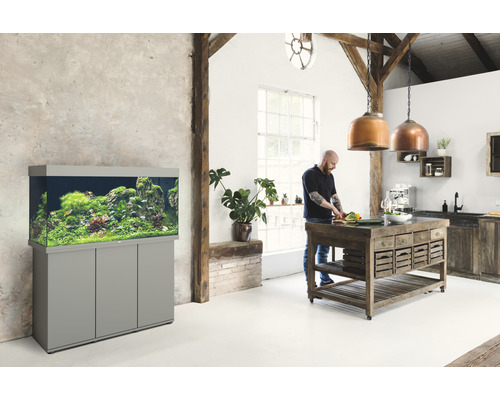 Wohnraum mit Aquarium auf Unterschrank, Mann beim Zubereiten von Speisen