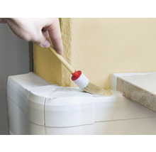 Hand streicht mit einem runden Pinsel Farbe auf eine Wand.