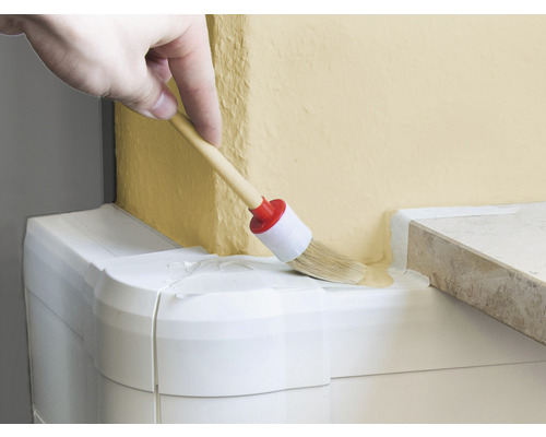 Hand streicht mit einem runden Pinsel Farbe auf eine Wand.