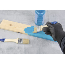 Eine Person streicht ein Holzbrett mit einem Pinsel und Farbe.