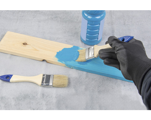 Eine Person streicht ein Holzbrett mit einem Pinsel und Farbe.