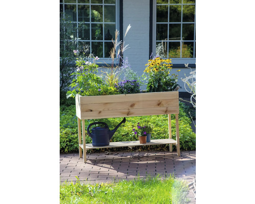 Hochbeet aus Holz mit Pflanzen, Gießkanne und Töpfen im Garten