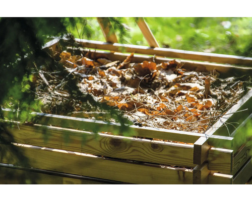 Holzkomposter gefüllt mit Laub und Ästen im Garten.