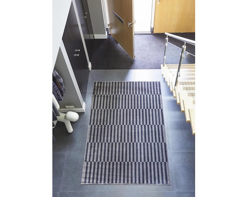Innenaufnahme eines Flurs mit einer rechteckigen Fußmatte mit Streifenmuster.