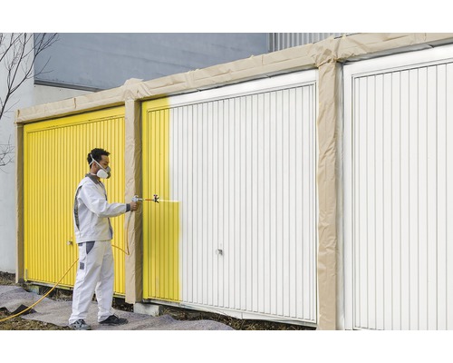 Mann sprüht Garagentor mit Farbspritzpistole