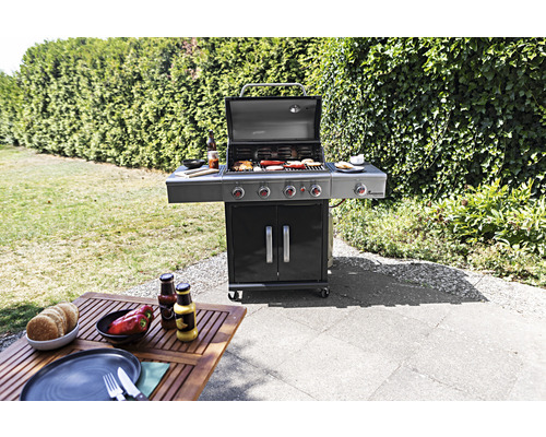 Gasgrill mit Grillgut auf einer Terrasse neben einem Tisch mit Lebensmitteln