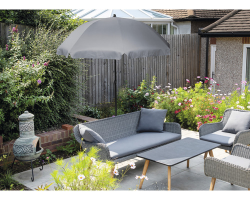 Gartenszene mit grauem Sonnenschirm, Rattansitzgruppe und Lehmofen auf einer Terrasse