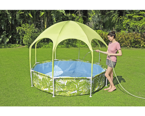 Garten Szene mit einem Frame Pool mit Blätter Muster und Sonnenschutzdach, während eine Frau den Pool mit einem Gartenschlauch befüllt.