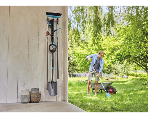 Gartenszene mit Werkzeug Wandhalterung, Spaten, Besen, Gartenschlauch und Gießstab