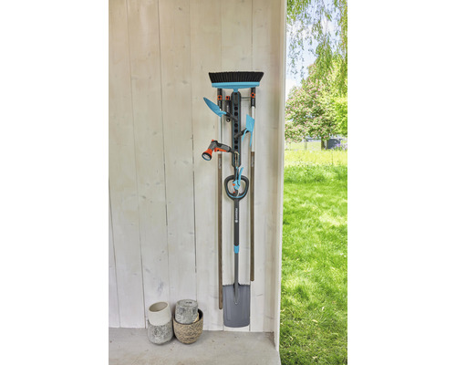 Gartengerätehalter an einer Wand mit Gartengeräten wie Spaten, Besen und Gartenschlauch