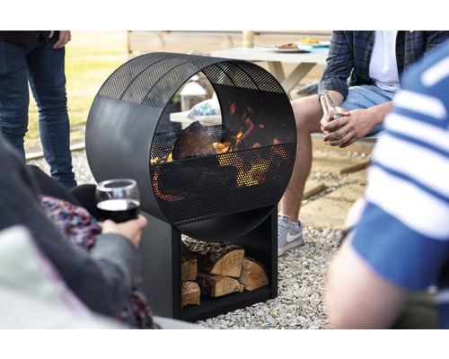 Kreisförmige Feuerstelle aus Metall mit Holzscheitlager im Garten mit Personen