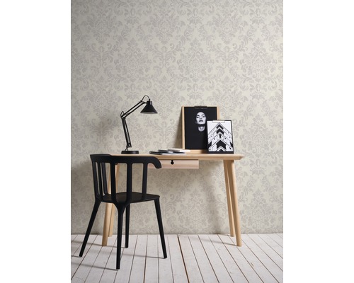 Ein Arbeitszimmer mit einem Schreibtisch, einem Stuhl, einer Lampe und einer Tapete mit floralem Muster.