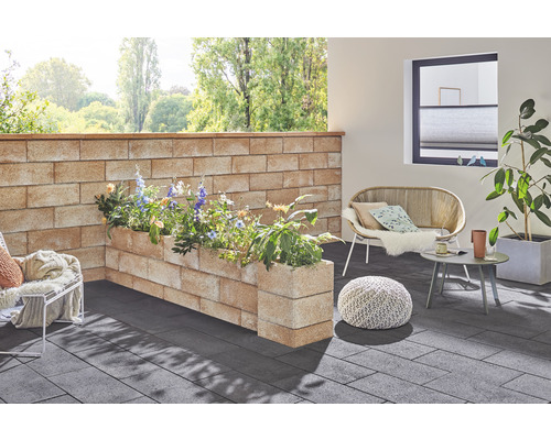 Gestalteter Außenbereich mit Mauer, Pflanzkästen, Sitzgelegenheiten und Bodenbelag.