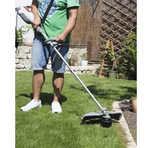 Eine Person benutzt einen Rasentrimmer im Garten, um Rasen zu schneiden.
