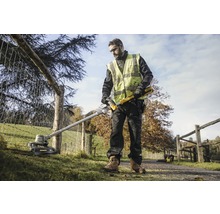 Ein Mann bedient einen Rasentrimmer von DeWalt in einem Garten nahe eines Zauns.