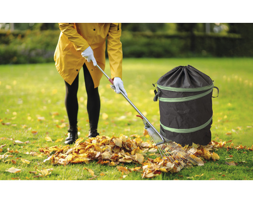 Frau räumt Laub mit einem Rechen und einem Gartensack auf