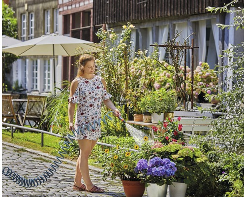 Frau gießt Blumen mit einem Gartenschlauch im Garten.