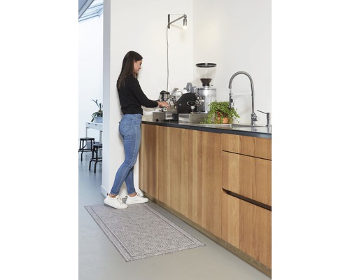 Frau bereitet Kaffee in einer hellen Küche mit einem Küchenteppich