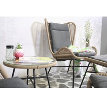 Szene mit Rattansessel, grauem Kissen und Beistelltisch mit Glasplatte