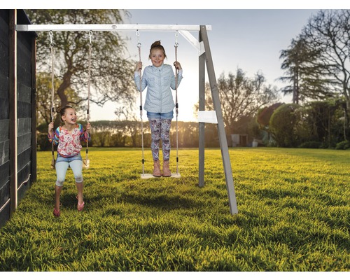 Zwei Kinder schwingen auf einer Holzschaukel im Garten.