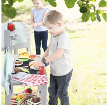 Kinder spielen mit einem hölzernen Spielzeuggrill im Garten, inklusive Spielzeuglebensmitteln