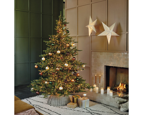 Dekorierter Weihnachtsbaum mit Lichtern und Kugeln im Wohnzimmer neben einem Kamin.