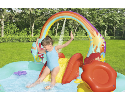 Planschbecken mit Rutsche und Regenbogen-Wassersprüher im Garten mit spielendem Kind.