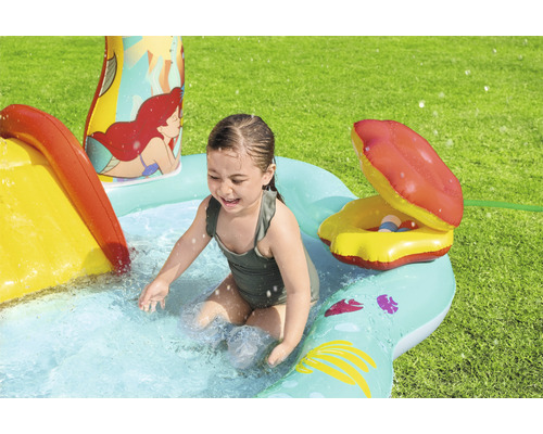 Mädchen spielt im aufblasbaren Planschbecken mit Rutsche und Wassersprinkler