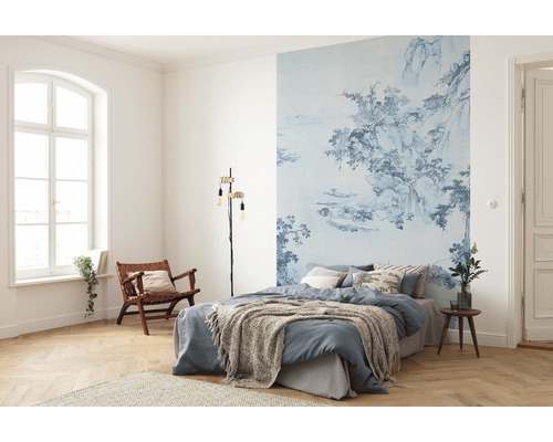 Schlafzimmer mit blau gemusterter Fototapete, Bett, Leselampe und Holzstuhl