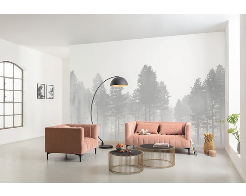 Wohnzimmer mit Sofa, Sessel, Stehlampe und Couchtischen vor einer Fototapete mit Waldmotiv.