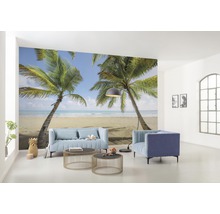 Wohnraum mit Fototapete, die eine tropische Szene mit Palmen und Strand zeigt, mit Möbeln wie Sofa und Sesseln.