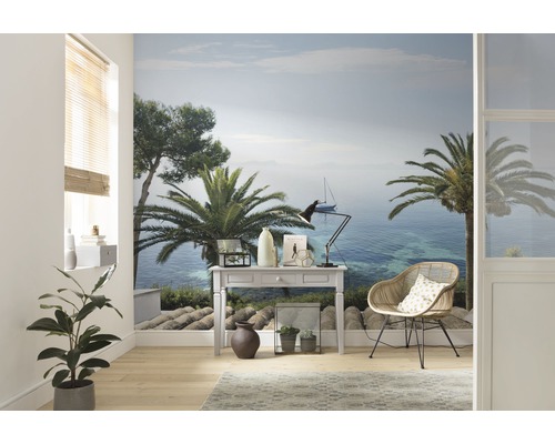 Wohnraum mit Fototapete, die eine Küstenlandschaft mit Palmen und einem Segelboot zeigt, eingerichtet mit einem Schreibtisch und einem Rattansessel.