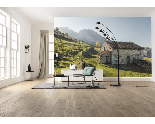 Wohnzimmer mit Fototapete eines Steinhauses in einer grünen Hügellandschaft