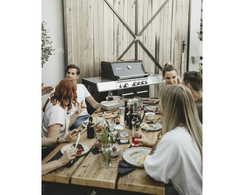 Gruppe von Personen sitzt an einem Holztisch mit einem Gasgrill im Hintergrund