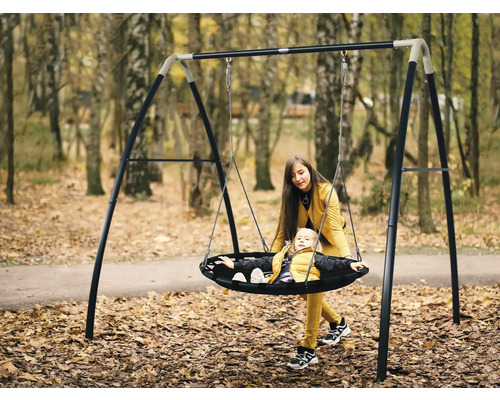Mutter schiebt Kind auf einer Nestschaukel mit Stahlrahmen im Garten