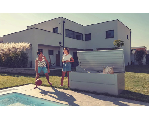 Szene im Freien mit einer offenen Aufbewahrungsbox auf einer Rasenfläche neben einem Pool, mit zwei Personen und einem Haus im Hintergrund