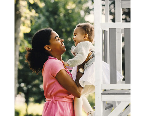Eine Frau hält ein Kind neben einem Spielturm im Garten.