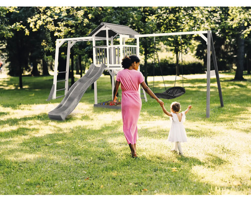 Spielplatz mit Turm, Rutsche und Schaukel im Garten, eine Frau hält die Hand eines Kindes