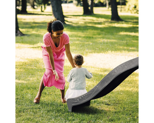 Eine Frau mit einem Kind an einer Kinderrutsche auf einer Wiese.