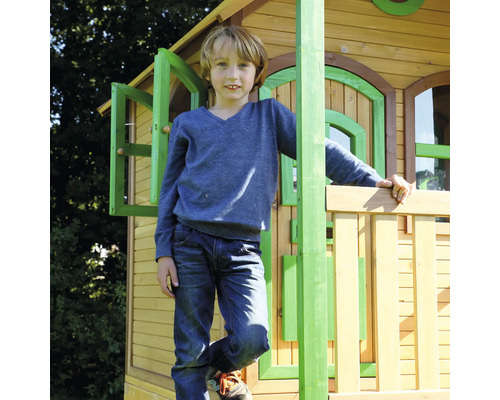 Junge steht auf einem Holzspielhaus mit Fenstern und Geländer
