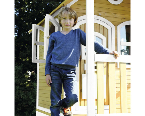 Junge steht vor einem Holzspielhaus mit geöffneten Fenstern