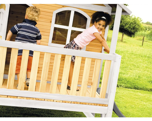 Kinder spielen in einem Holzspielhaus mit Rutsche im Garten.