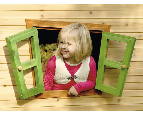 Mädchen schaut aus einem Holzspielhausfenster mit grünen Fensterläden.