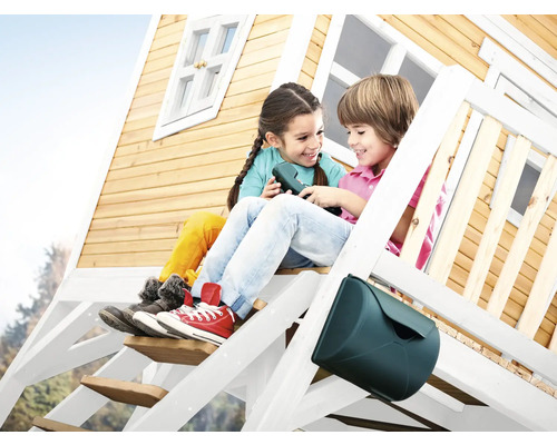 Zwei Kinder sitzen auf der Treppe eines Holzspielhauses mit Briefkasten.