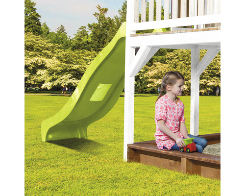 Kind sitzt in Sandkiste unter Spielturm mit Rutsche im Garten