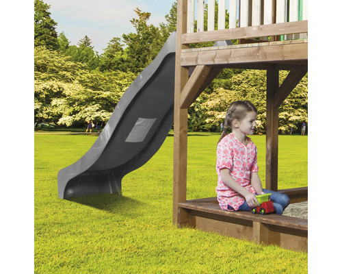 Spielturm mit Rutsche und spielendem Kind im Sandkasten