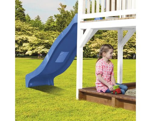 Mädchen sitzt auf einer Sandkiste unter einem Spielturm mit Rutsche